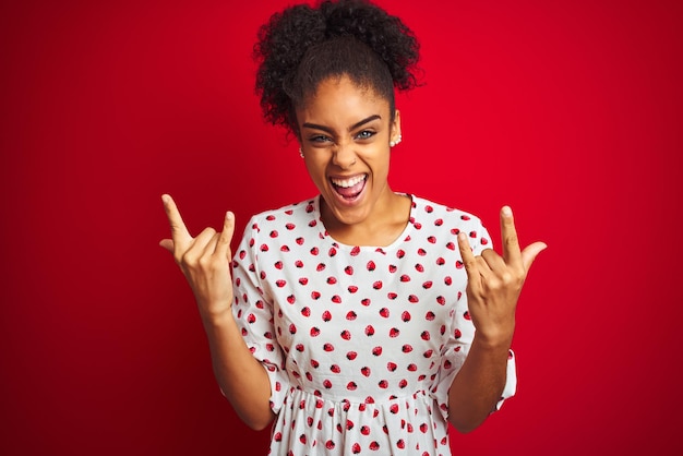 African american woman wearing fashion white dress standing over isolated red background shouting with crazy expression doing rock symbol with hands up Music star Heavy concept