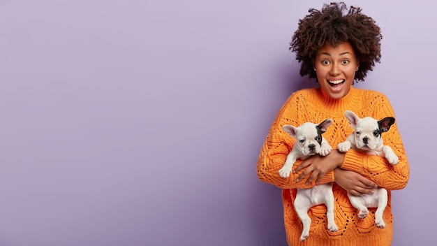 African American woman wearing orange sweater holding puppies