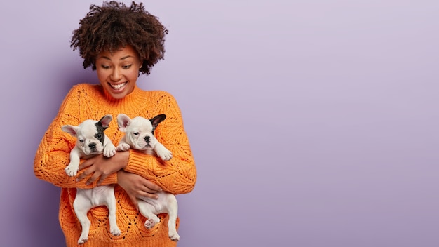 African American woman wearing orange sweater holding puppies