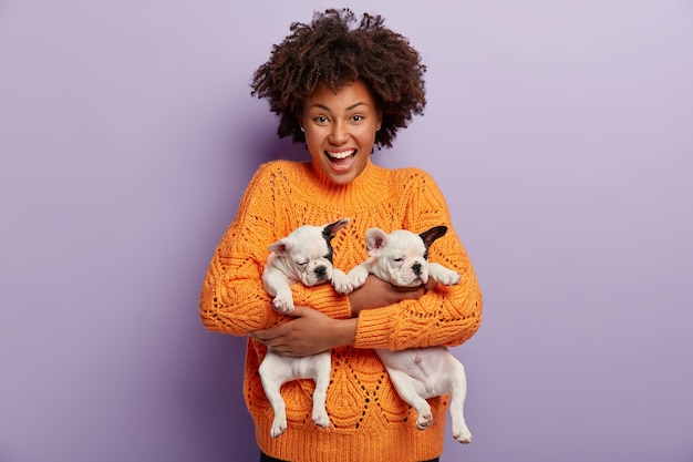 African American woman wearing orange sweater holding puppies