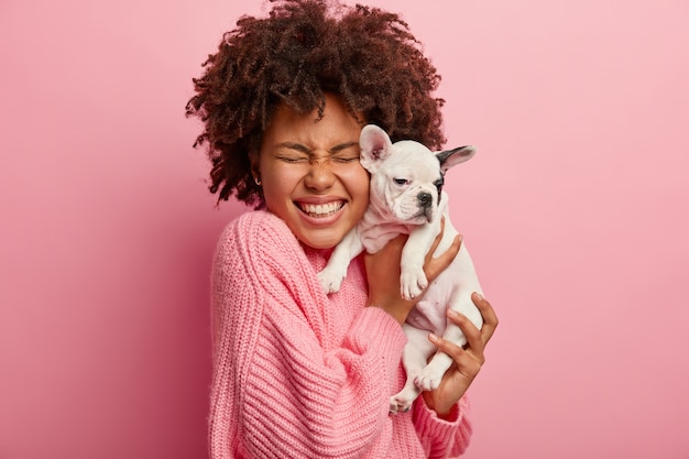 African American woman wearing pink sweater holding puppy
