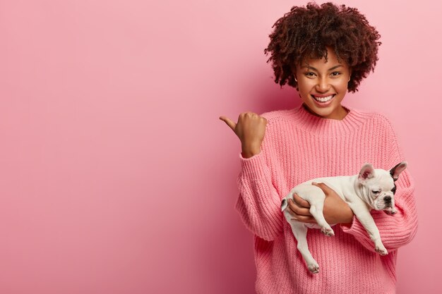 African American woman wearing pink sweater holding puppy