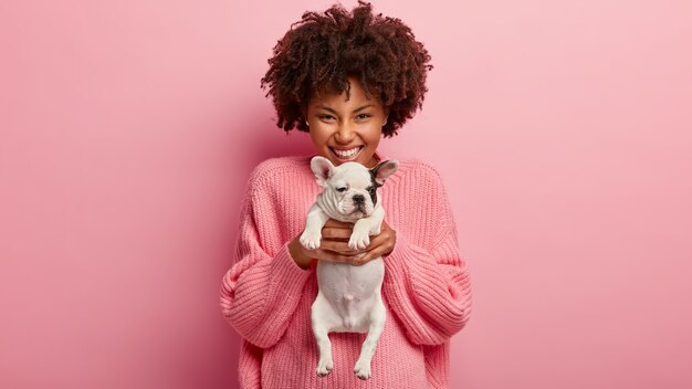 African American woman wearing pink sweater holding puppy