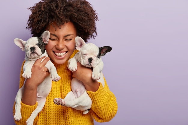 African American woman wearing yellow sweater holding puppies