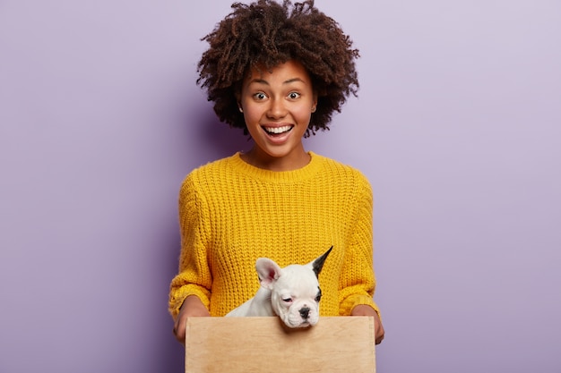 African American woman wearing yellow sweater holding puppy