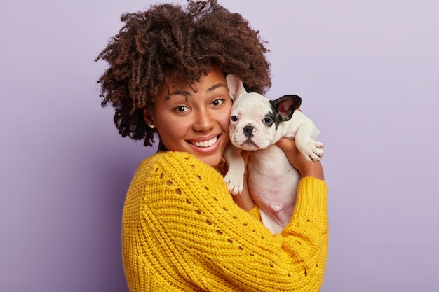 African American woman wearing yellow sweater holding puppy