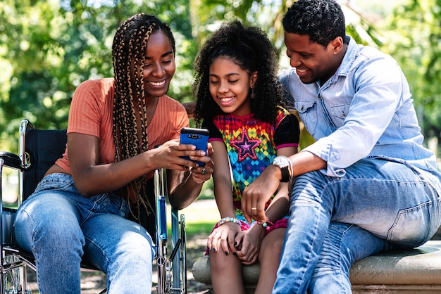 An african american woman in a wheelchair enjoying a day at the park with her family while using a mobile phone together