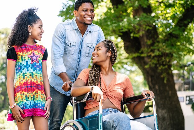Афро-американская женщина в инвалидной коляске, наслаждаясь прогулкой на открытом воздухе со своей дочерью и мужем.