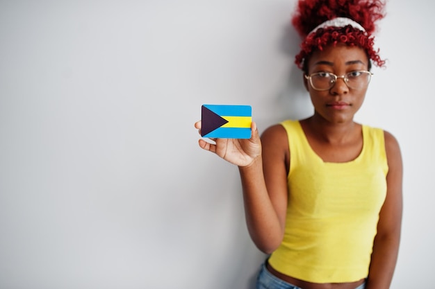 Foto gratuita la donna afroamericana con i capelli afro indossa la canottiera gialla e gli occhiali tengono la bandiera delle bahamas isolata su sfondo bianco