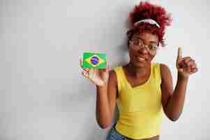 Free photo african american woman with afro hair wear yellow singlet and eyeglasses hold brazil flag isolated on white background show thumb up