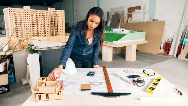 Free photo african american woman with model of house on table near safety helmet and equipments