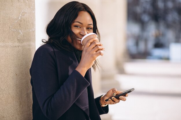 コーヒーを飲みながら携帯電話を持つアフリカ系アメリカ人女性