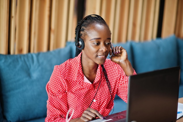 La donna afroamericana lavora in un operatore di call center e un agente del servizio clienti che indossa cuffie con microfono che lavorano su laptop