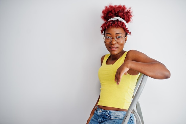 African american woman in yellow singlet and eyglasses against white wall stand om iron ladder