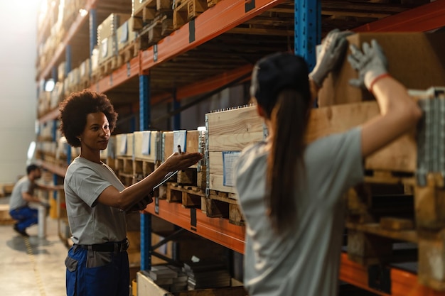 Operaio afroamericano che comunica con la sua collega mentre prepara la spedizione in un magazzino industriale