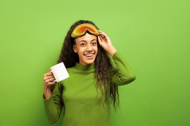 Портрет афро-американской молодой брюнетки в лыжной маске на зеленом пространстве