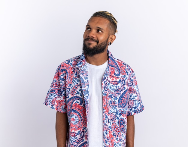 Free photo african american young man in colorful shirt looking aside smiling cheerfully happy and positive standing over white