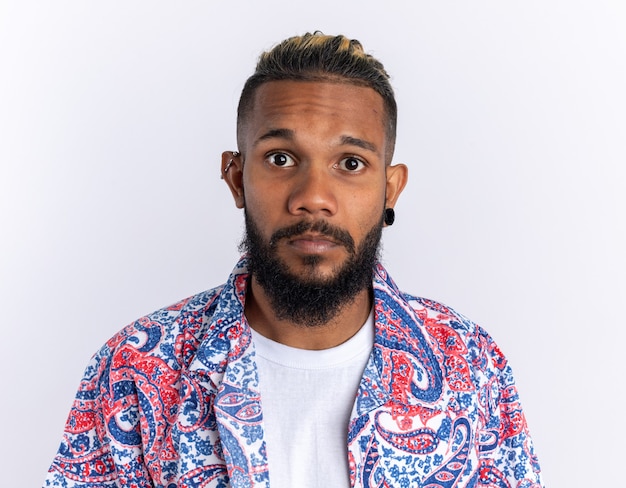 Free photo african american young man in colorful shirt looking at camera puzzled standing over white background