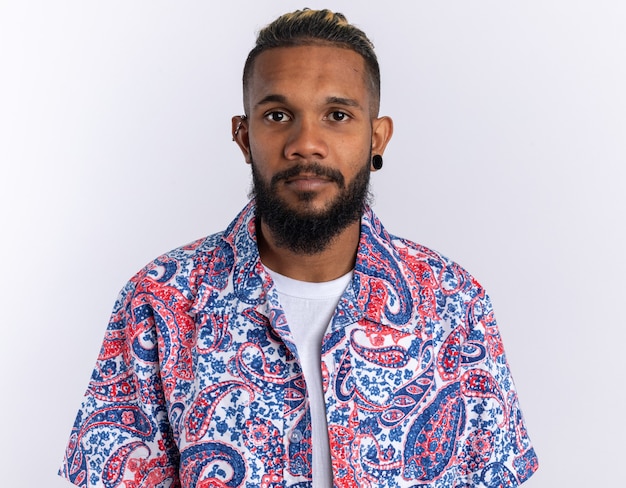 Free photo african american young man in colorful shirt looking at camera with serious confident expression standing over white background