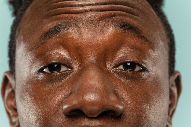 African-american young man's close up portrait on blue studio background. Beautiful male model with well-kept skin. Concept of human emotions, facial expression, sales, ad. Eyes and cheeks.