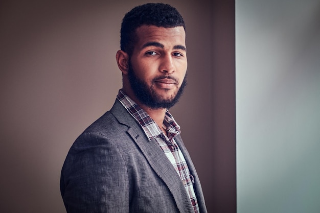 Free photo african-american young man wearing a jacket and checkered shirt looking at a camera in a studio.