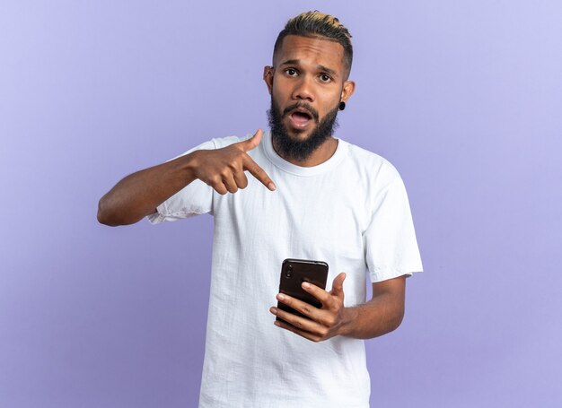 African american young man in white t-shirt holding smartphone pointing