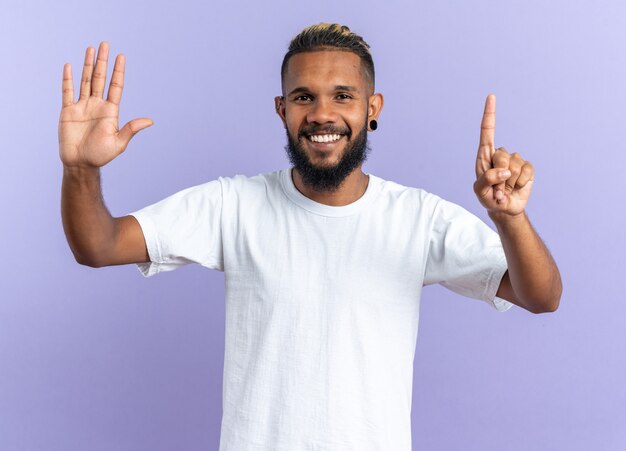 African american young man in white t-shirt looking at camera smiling cheerfully showing number six with fingers