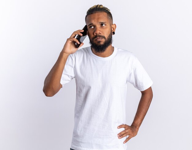 휴대 전화로 이야기하는 동안 혼란 스 러 워 보이는 흰색 티셔츠에 아프리카 계 미국인 젊은 남자