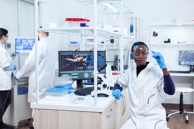 彼女​の​職場​に​座っている​スライド​ガラス上​の​サンプル​を​見ている​アフリカ​の​生化学​。​滅菌​装置​を​身​に​着けている​生化学​実験室​の​黒人​医療​科学者​。