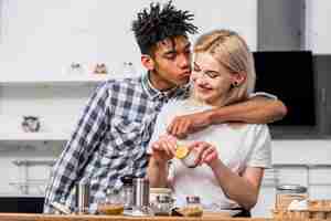 Free photo an african boyfriend kissing her smiling girlfriend preparing food in the kitchen