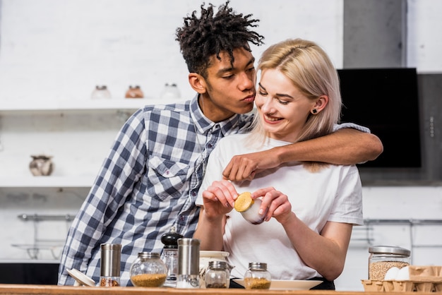 An african boyfriend kissing her smiling girlfriend preparing food in the kitchen