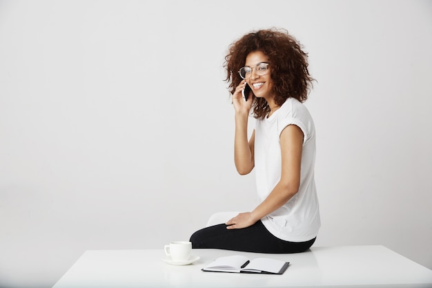 Donna di affari africana che ride parlando al telefono sul posto di lavoro, ricevendo una telefonata dal suo manager sull'arte che fa.