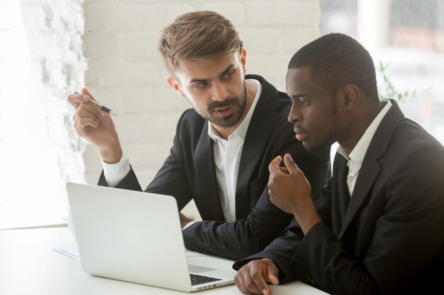 African and caucasian businessmen discussing online project idea with laptop