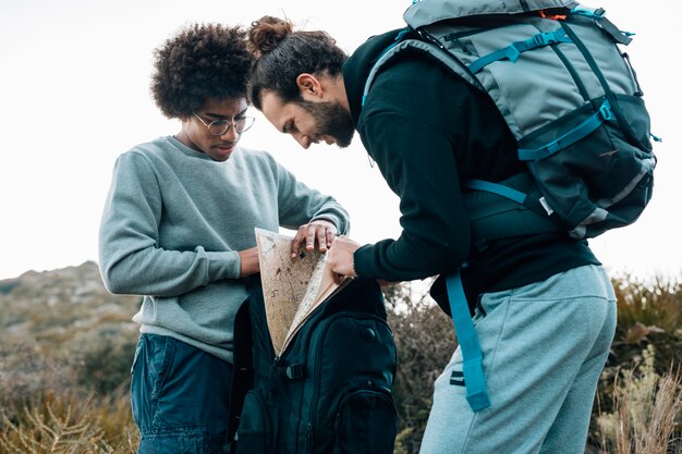 An african and caucasian young men looking for map in the backpack