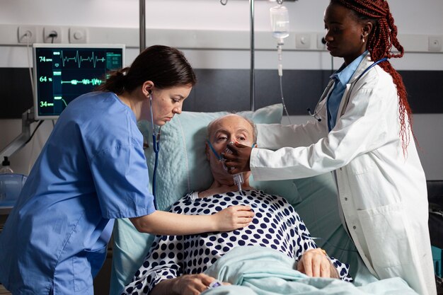 African doctor and medical assistant helping senior man breath using oxygen mask, in hospital laying in bed