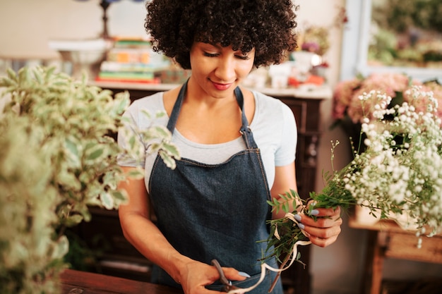 Free photo african female florist cutting string tied on bunch of flowers