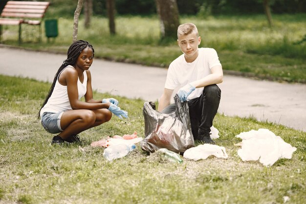 Африканская девочка и европейский мальчик собирают мусор. Активисты расчищают парк боком.
