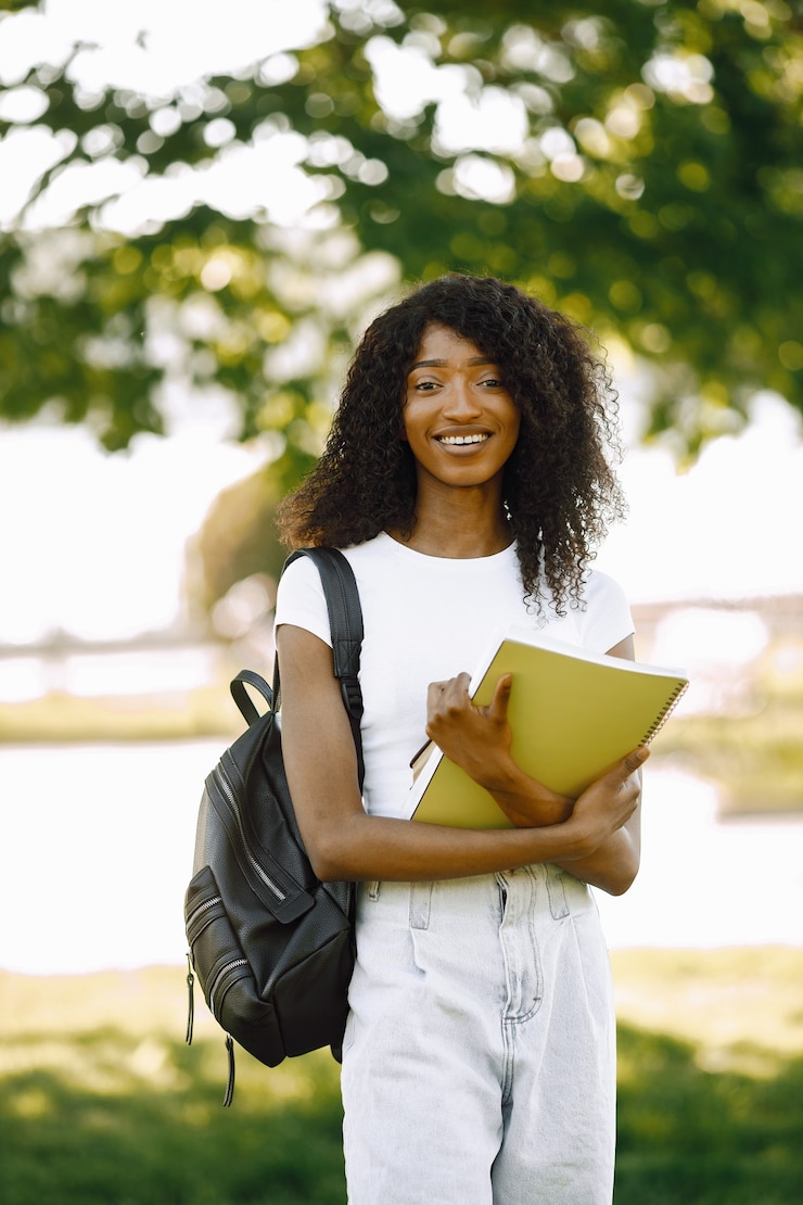 Free Photo african girl holding a books for studying while standing oudoors. girl is looking directly at camera