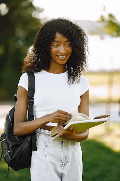 Free photo african girl holding a books for studying while standing oudoors. girl is reading book