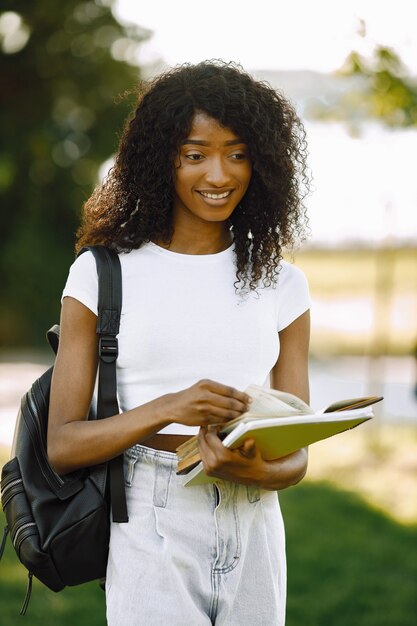 African girl holding a books for studying while standing oudoors. Girl is reading book