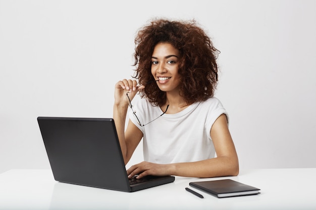 African girl smiling  sitting at wokplace with laptop.