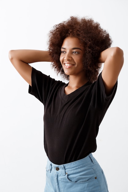 African girl smiling with hands behind head over light wall.