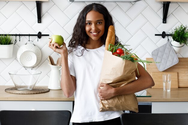 Африканская девушка стоит на кухне и держит бумажный пакет с продуктами