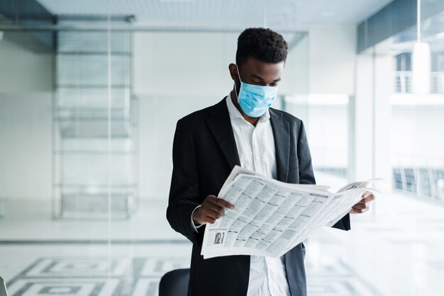 Африканский красивый деловой человек в медицинской маске, читая газету в офисном здании