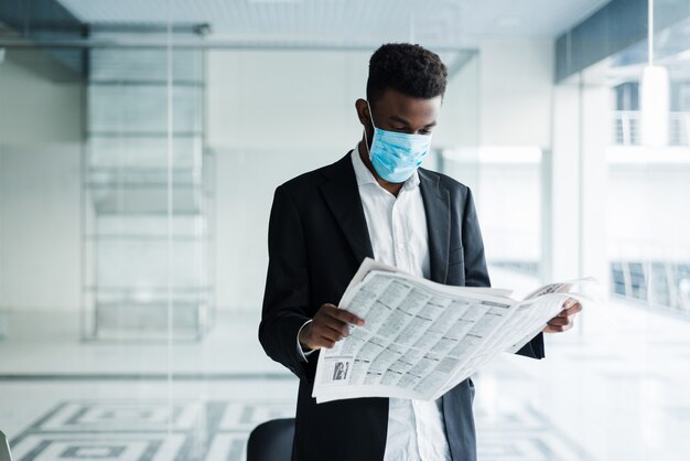 African handsome business man in medical mask reading the newspaper at office building