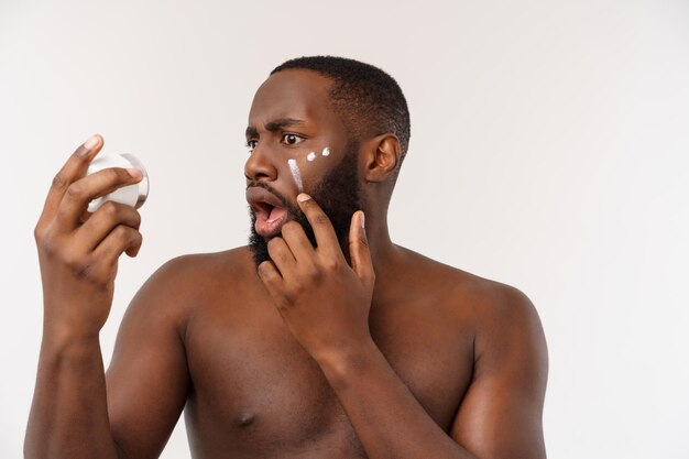 Африканский красавец наносит крем на лицо мужская концепция ухода за кожей