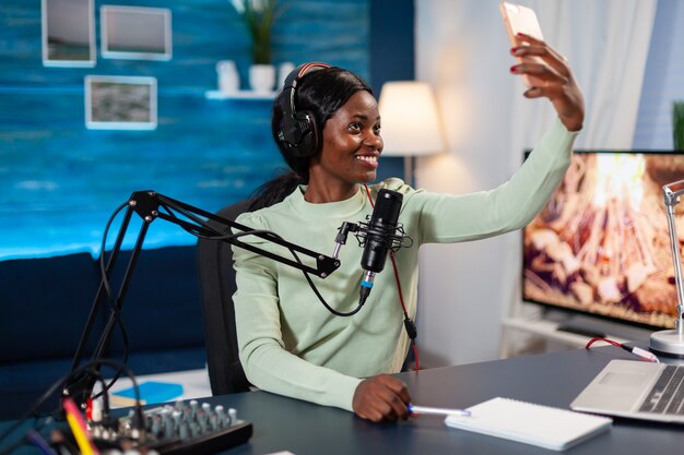 African influencer recording podcast and taking selfie in home studio. On-air online production internet podcast show host streaming live content, recording digital social media.