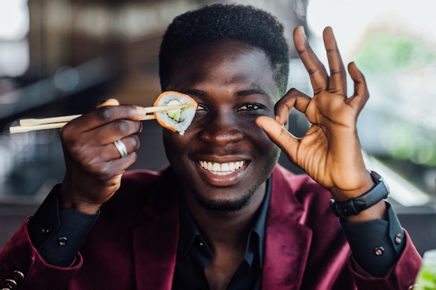 African male holding sushi under eye, break time in restaurant.