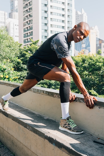 African male runner athletic stretching muscles on roof top