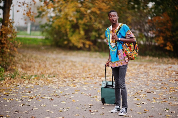 Free photo african man in africa traditional shirt on autumn park with backpack and suitcase emigrant traveler